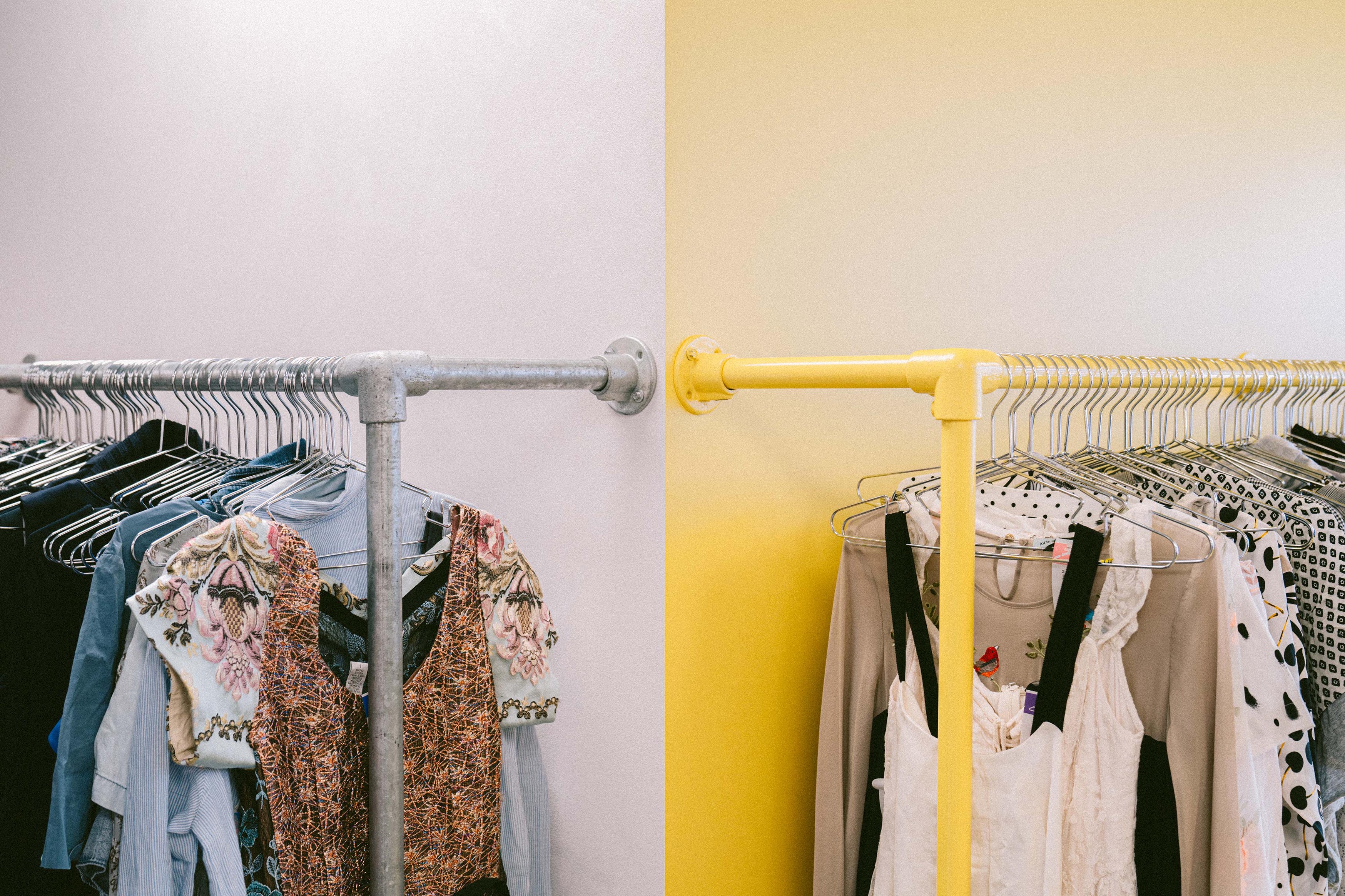 Clothing rack of secondhand dresses on yellow feature wall.